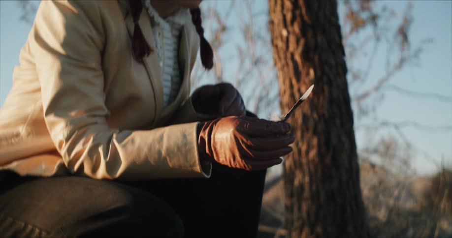 Young woman wearing gloves picks up a feather from the ground on the desert