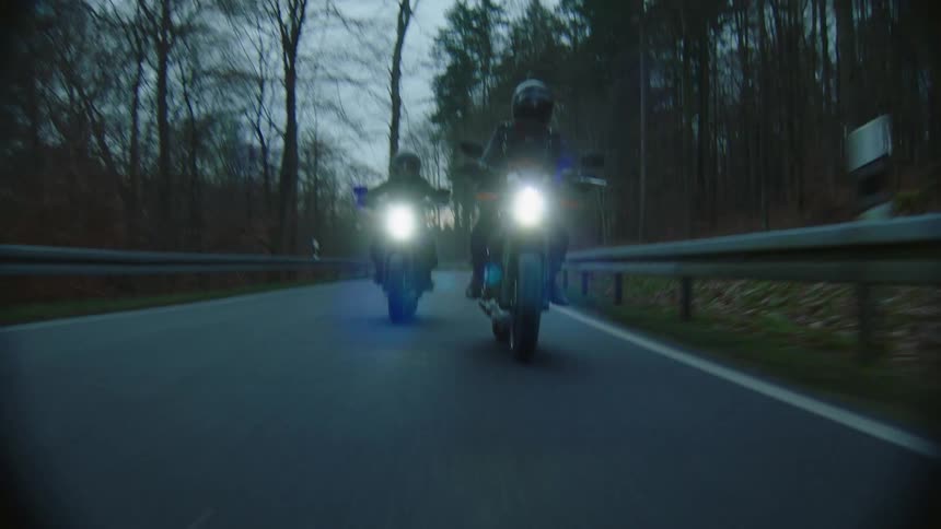 Two motorcyclist ride along highway through woods during the fall
