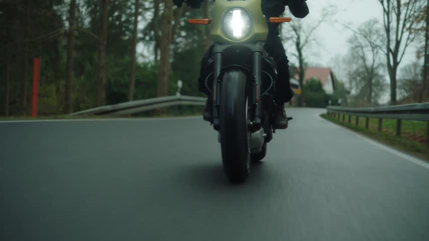 Motorcyclist rides motorcycle along highway past house and woods