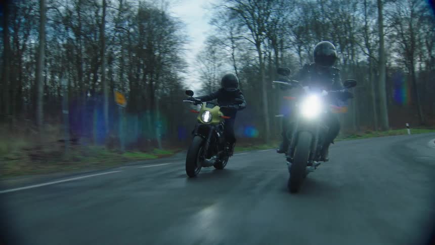 Two riders on motorcycles traveling on a curving road through the trees