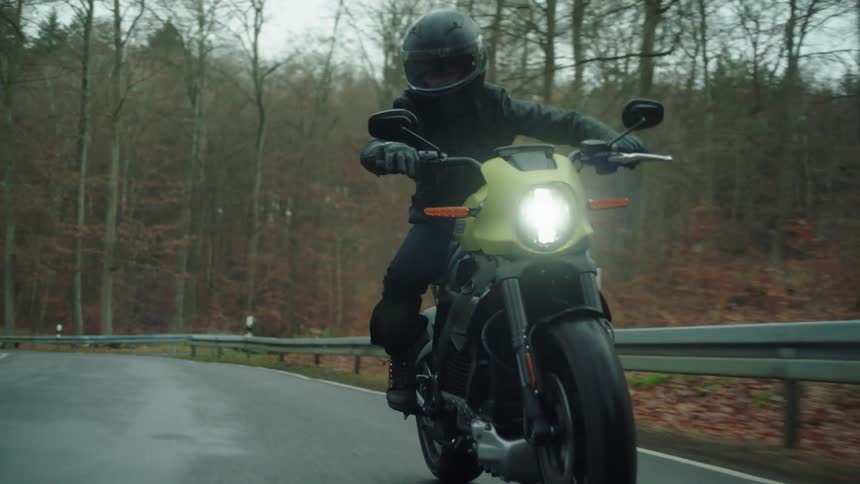 A motorcyclist rides a motorcycle along a road through a woodland on an autumn day