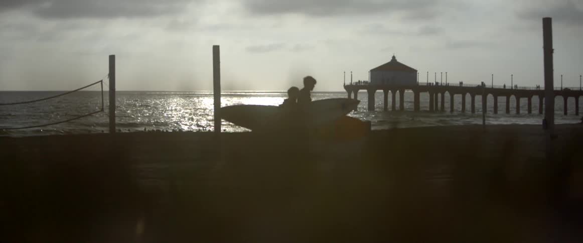 Two men carrying surfboards walk near the ocean