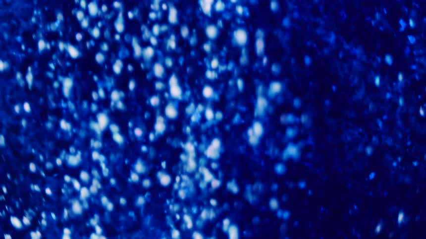 Small shiny spheres are falling and moving in an electric blue environment