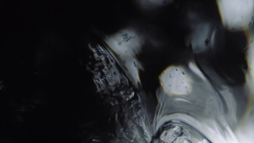 A clear liquid with translucent gray speckles ripples as it moves over soft glowing spheres