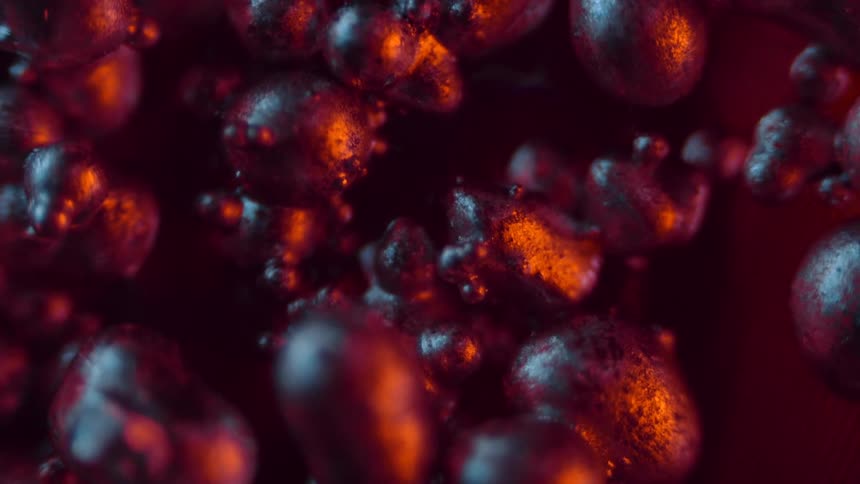 Red light shines on organic metal spheres stuck together as they move in the darkness