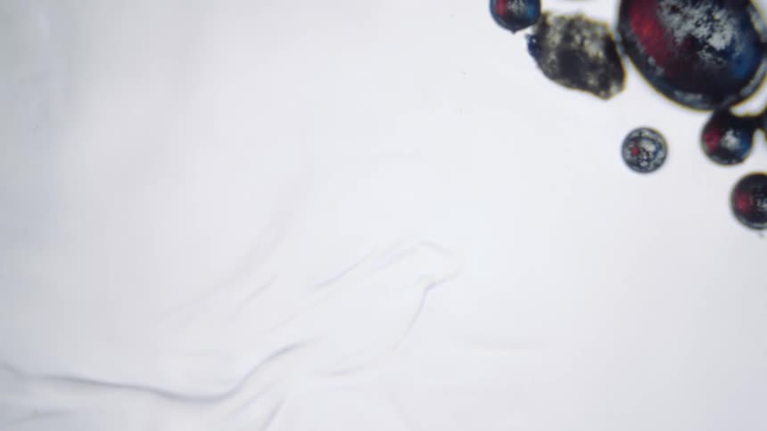 Black metal droplets sit in a white flowing liquid