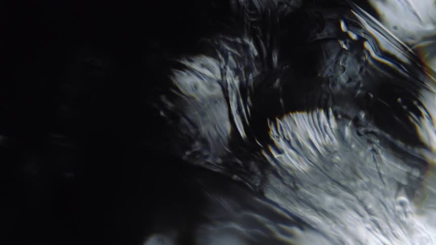 Light reflects on smokey clear liquid as it ripples and moves