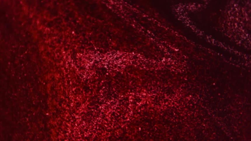 Illuminated particles glow as they move inside a red rippling substance