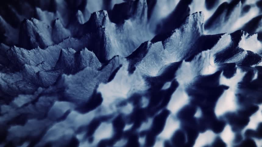 Light shines on spikes stretching from a textured surface as they move and bend in the shadows