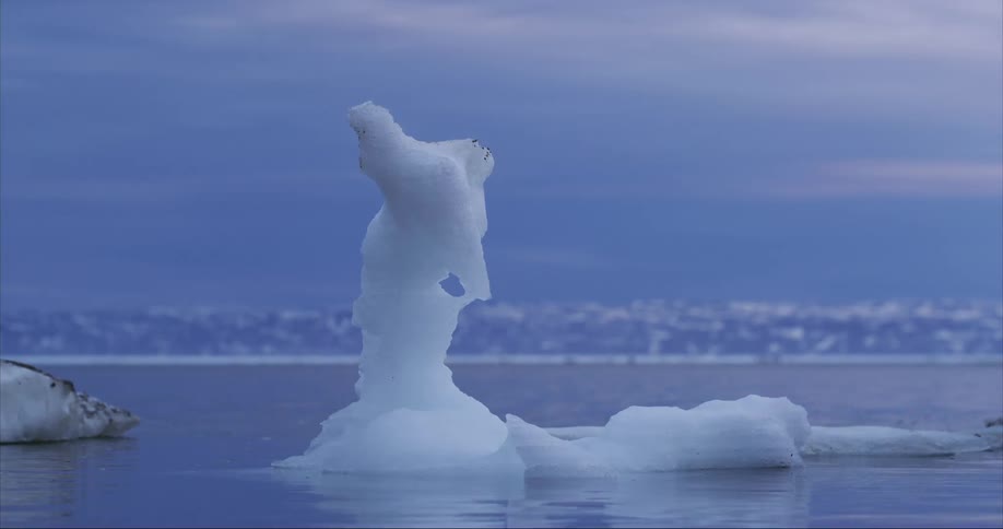 An mostly melted iceberg floats in sea water under the midnight sun