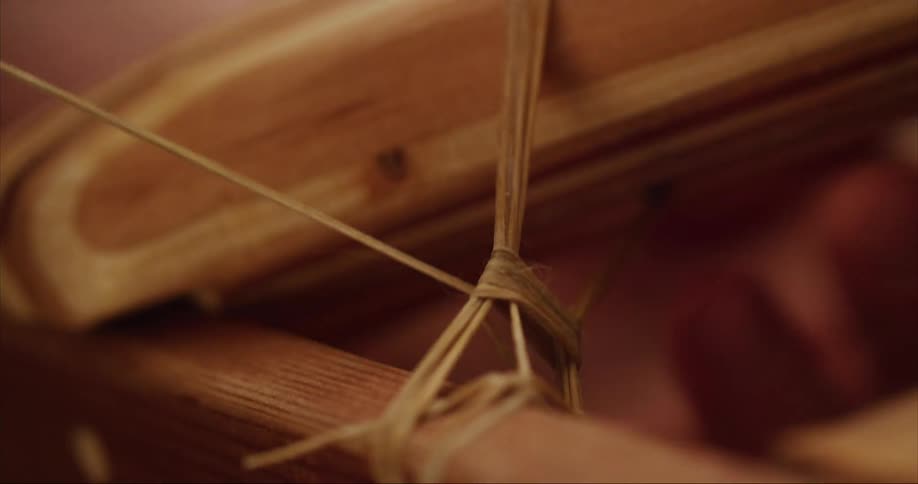 Close up view of a persons fingers as they wrap a string around pieces of wood and pull it as they build their traditional sea kayaks