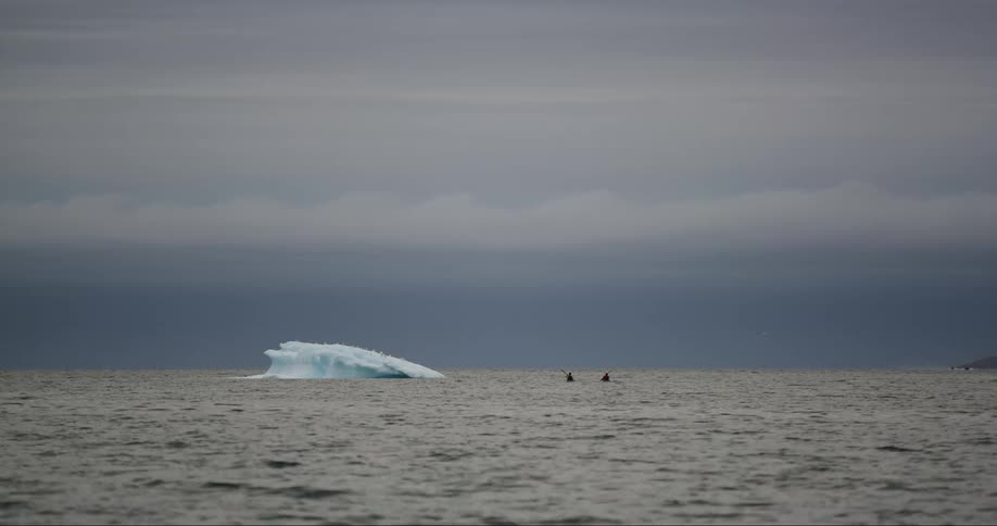 Two people paddle sea kayaks past a melting iceberg on Baffin Island in the Arctic Ocean