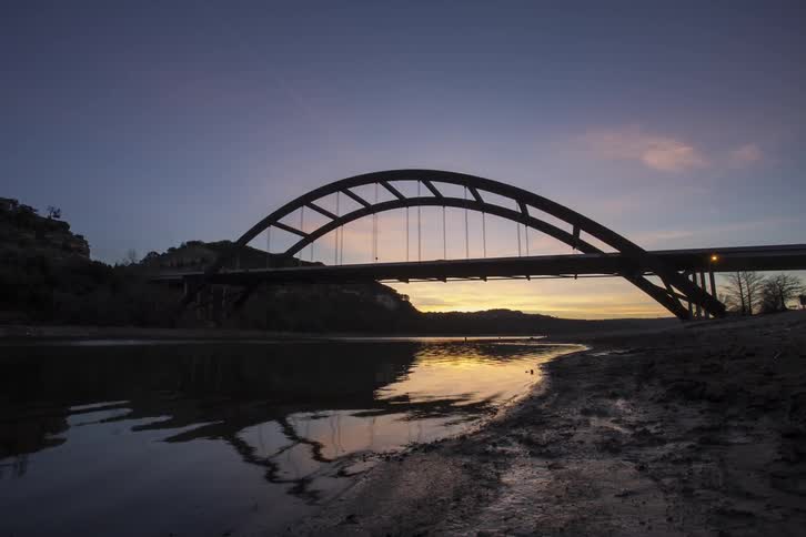 Clouds and move and the sun rises over a bridge and a river