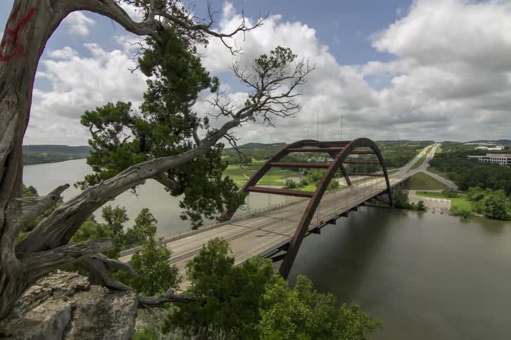 Traffic crossing a highway bridge that spans a river as clouds pass overhead