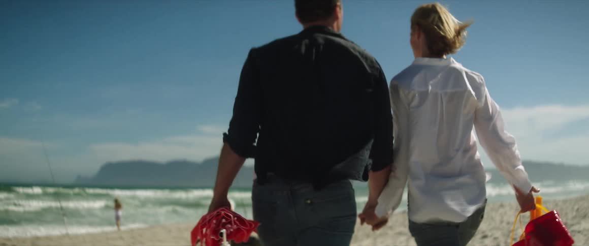 Man and woman wearing jeans white and black shirts walking on the beach holding hands