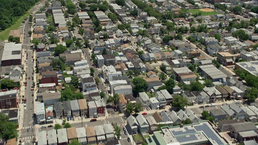 Aerial footage of urban Newark homes tilting to reveal and approach the Manhattan skyline in the background on a partly cloudy day