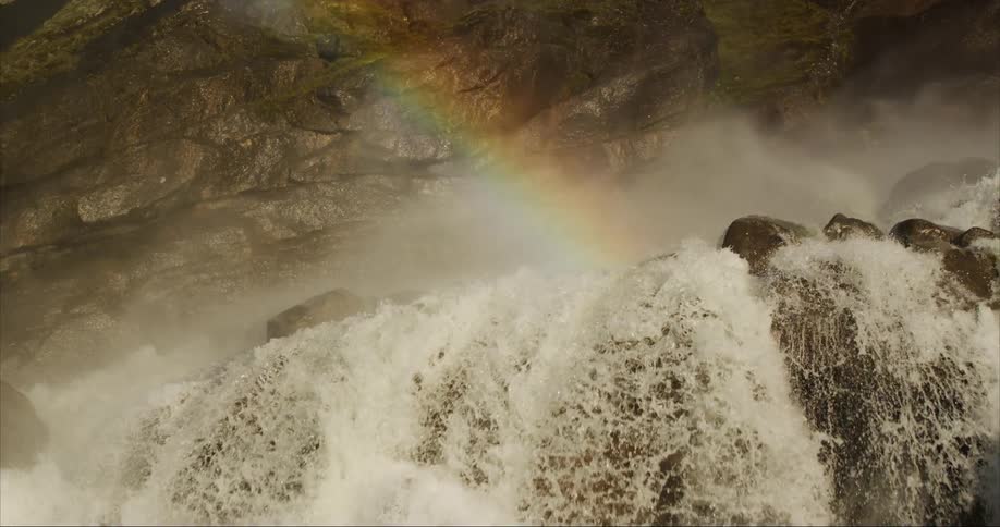 A rainbow is over the waterfall as the camera follows the current over the falls