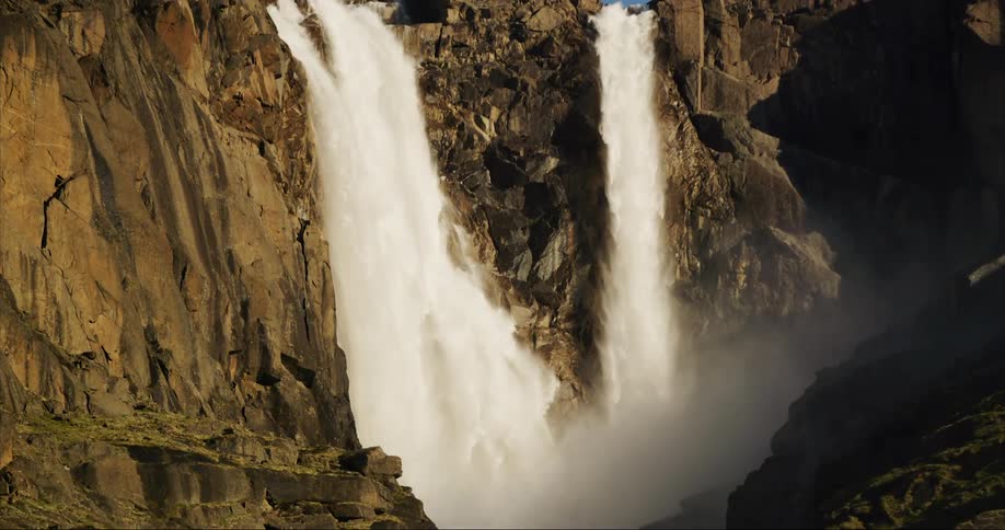 A giant waterfall tumbles from a glacier into a U-shaped valley below in this slow tilt down moment