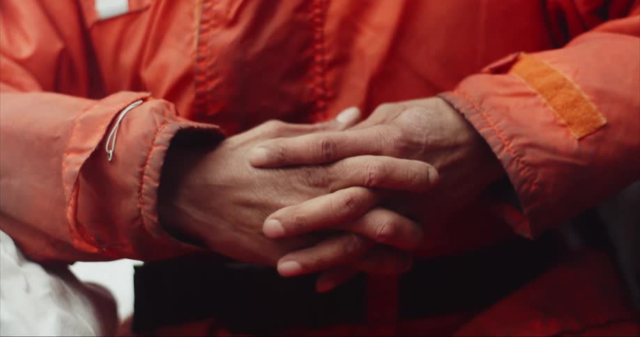 A crew member man holding his weathered hands together while taking orders from the boat captain