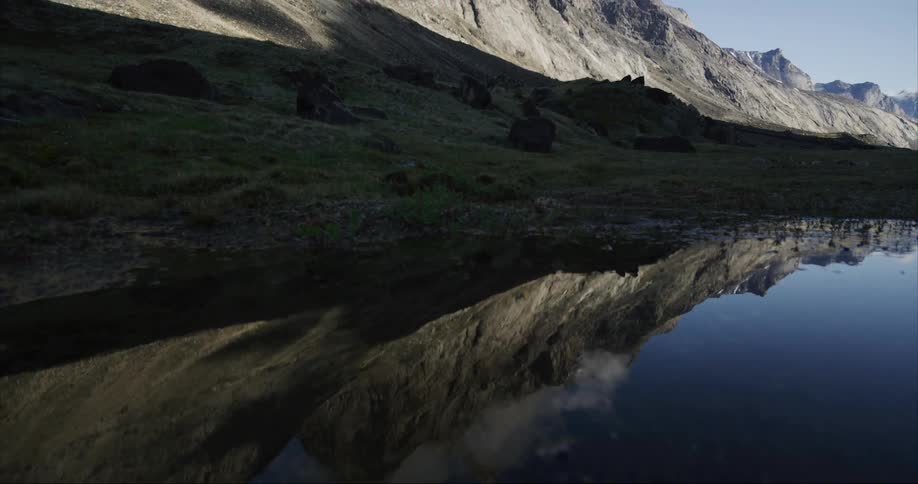 A calm reflective lake next to a granite mountain on Baffin Island, Nunavut