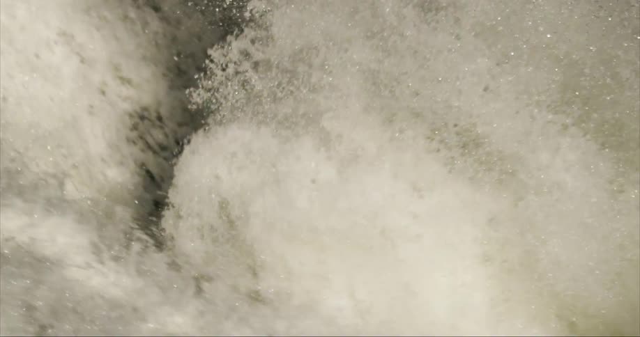 Water exploding into tiny droplets at the base of a massive waterfall in early morning light