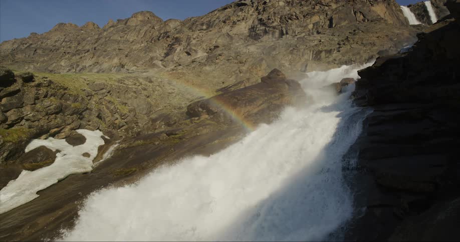 A massive waterfall cascades downhill with a brilliant rainbow illuminating the scene