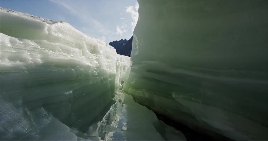 Crevice in glacier wall shows view of mountain under a cloudy and blue sky