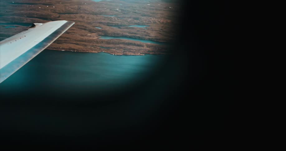 The view out an airplane window flying over a the Arctic Ocean and tundra of Baffin Island
