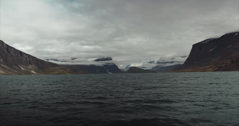 Clouds floating above snowy mountains as the boat cruises toward the expedition start point in the Arctic Ocean
