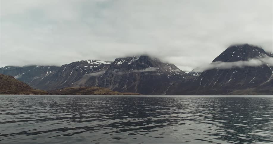 The Arctic Ocean ripples in the foreground with massive granite mountains laced with clouds in the background