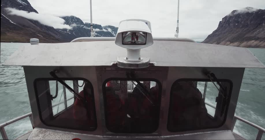 Bow point of view looking back at the captain as the fishing boat speeds towards the expedition start point with snow covered mountains in the background