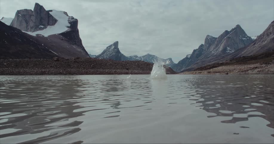 A stone is being thrown into glacier moraine alpine lake with glaciers, Mount Thor and other massive granite peaks in the background