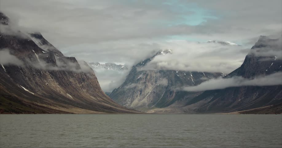 Clouds floating above snowy mountain peaks next to a lake