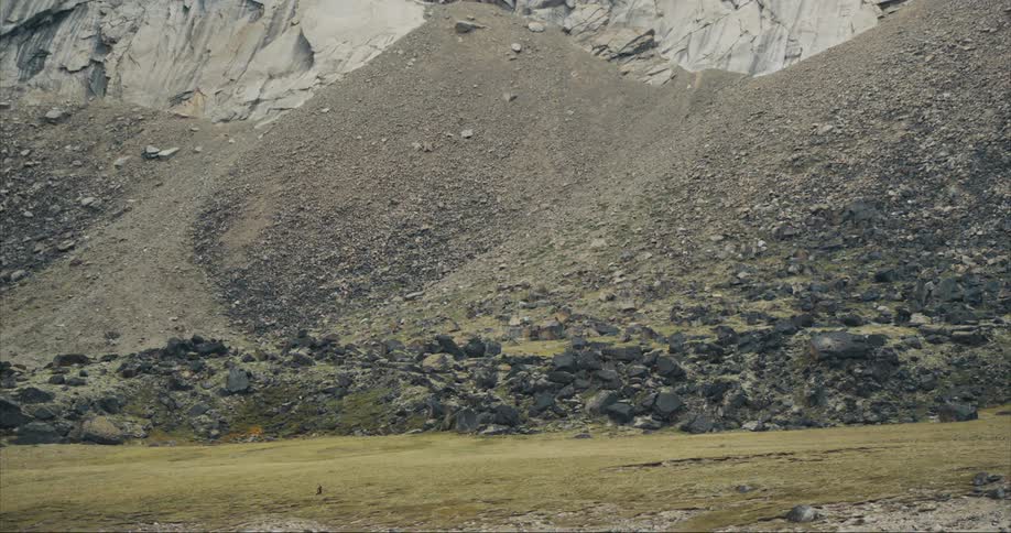 A person is walking across a field near the foot of a huge granite mountain on Baffin Island