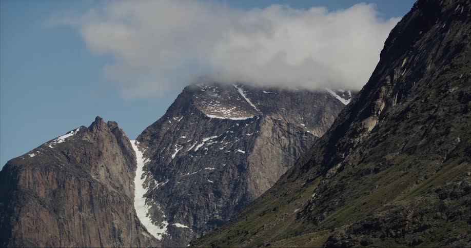 Low hanging storm clouds cling to a granite mountain covered in glaciers