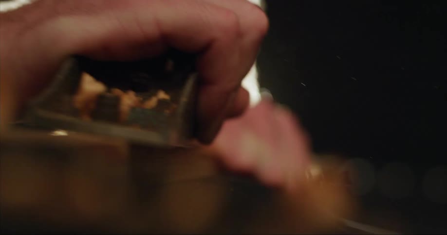 A male carpenter planing a piece of wood with a tool
