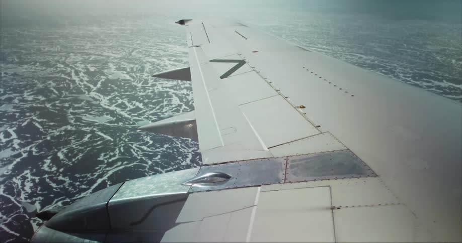 Light shines on the wing of an airplane as it flies high above the arctic tundra
