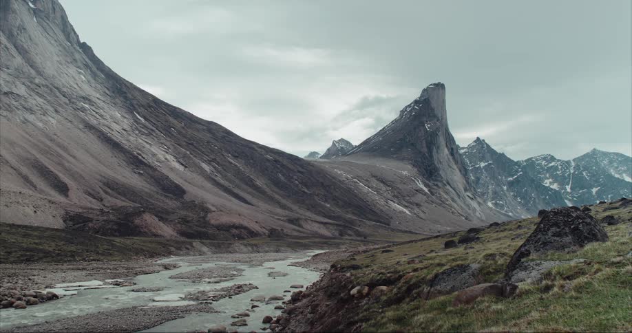 Mount Thor sits proudly on the skyline as a lone whitewater kayaker paddles down the arctic river
