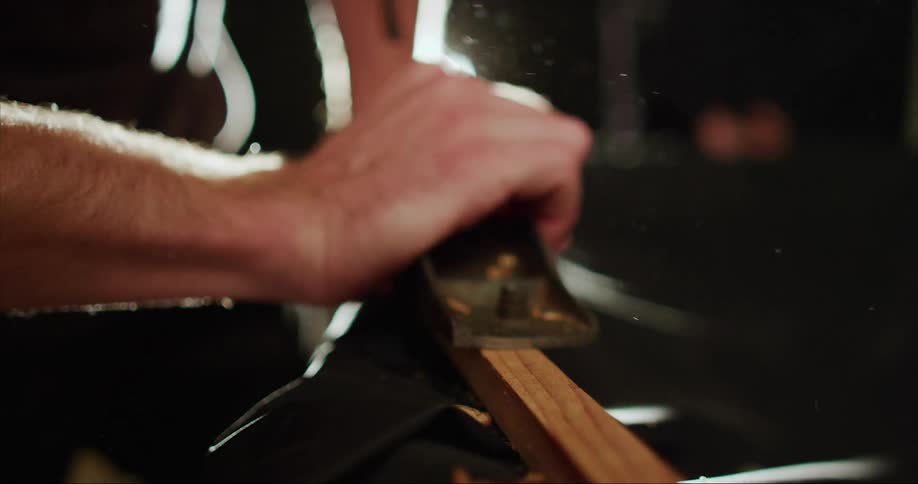 A male planing wood in a dark wood working shop