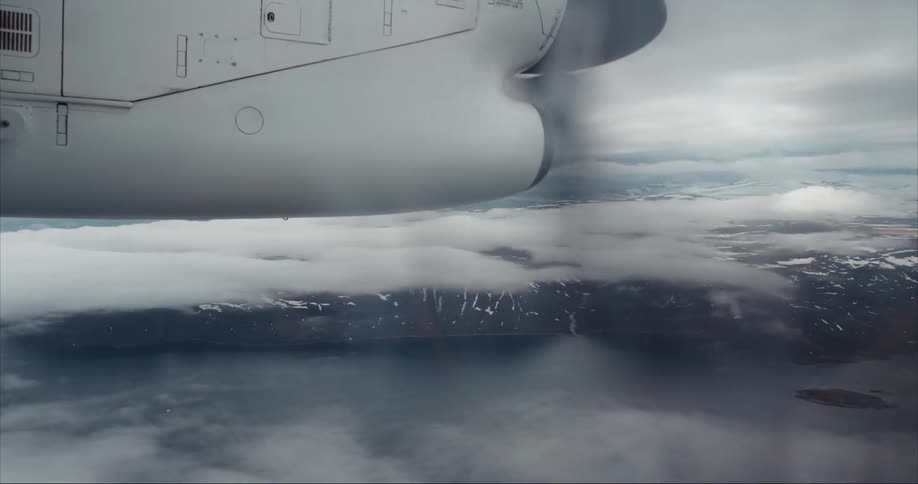 Twin engine prop Dash 8 airplane is flying above the Arctic Ocean and glacier covered mountains