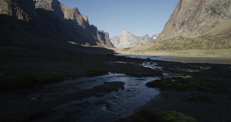 A small creek joins a bigger river with Mount Thor among granite mountains in a glacial river valley