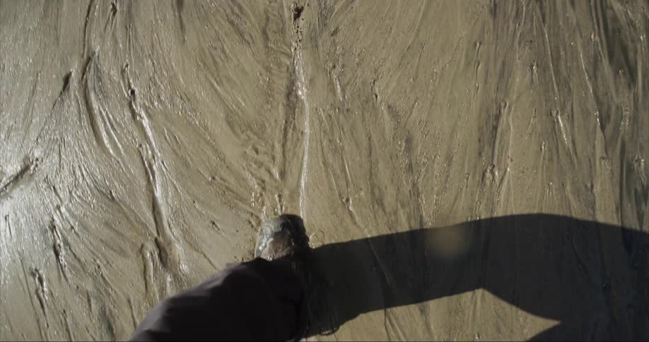 Person with dark pants and shoes walks through glacial sediment and sand