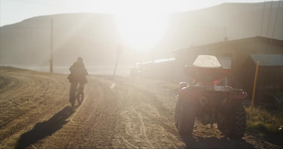A boy does a wheelie on his bike at sunset playing happily
