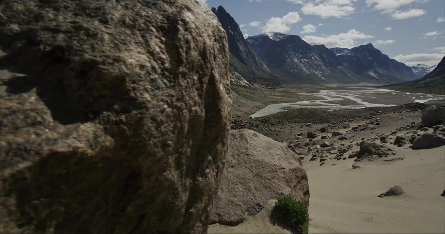 The camera dolly's past a massive granite boulder revealing an idyllic U-shaped glacier carved river valley