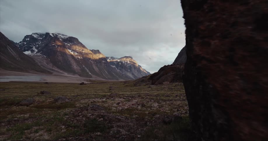 Camera moves past a large granite boulder revealing massive granite peaks, tundra and a glacier carved valley