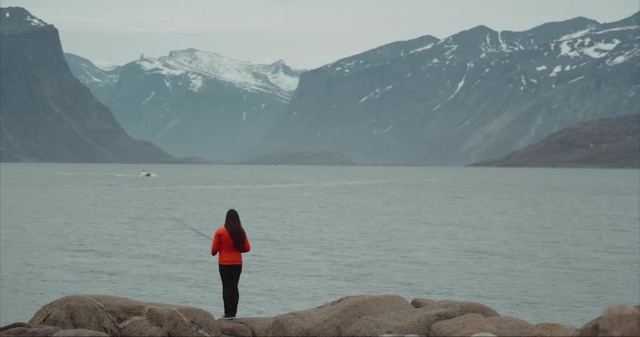A woman is fishing in the arctic sea near Pangnirtung on Baffin Island