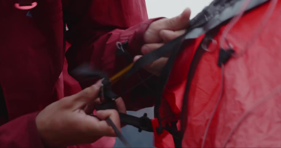 Man in red coat puts up red tent in the arctic circle on a windy and chilly night