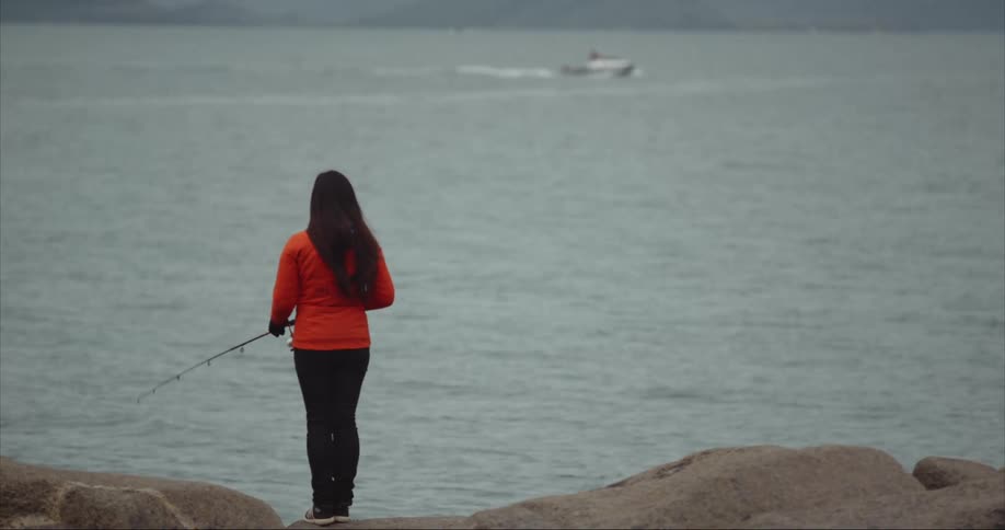 Woman wearing a bright orange jacket fishing on the coast of Baffin Island