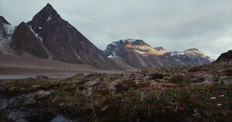 Heavy clouds hover over sharp icy mountain peaks in a glacier covered valley on Baffin Island