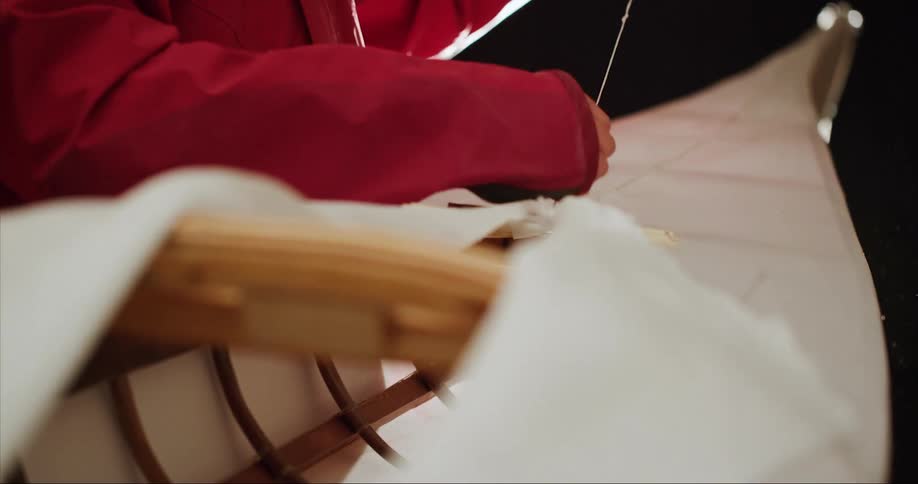 A person sewing canvas onto a traditional handmade wood frame Inuit style sea kayak